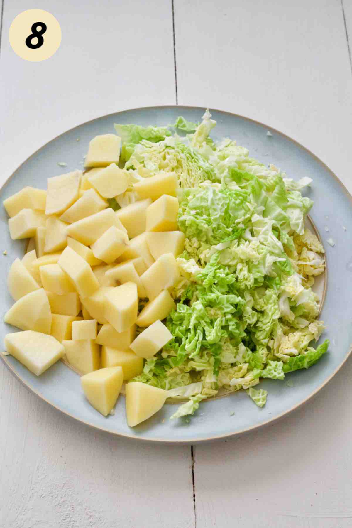 Plate with peeled and cubed potatoes and shredded cabbage.