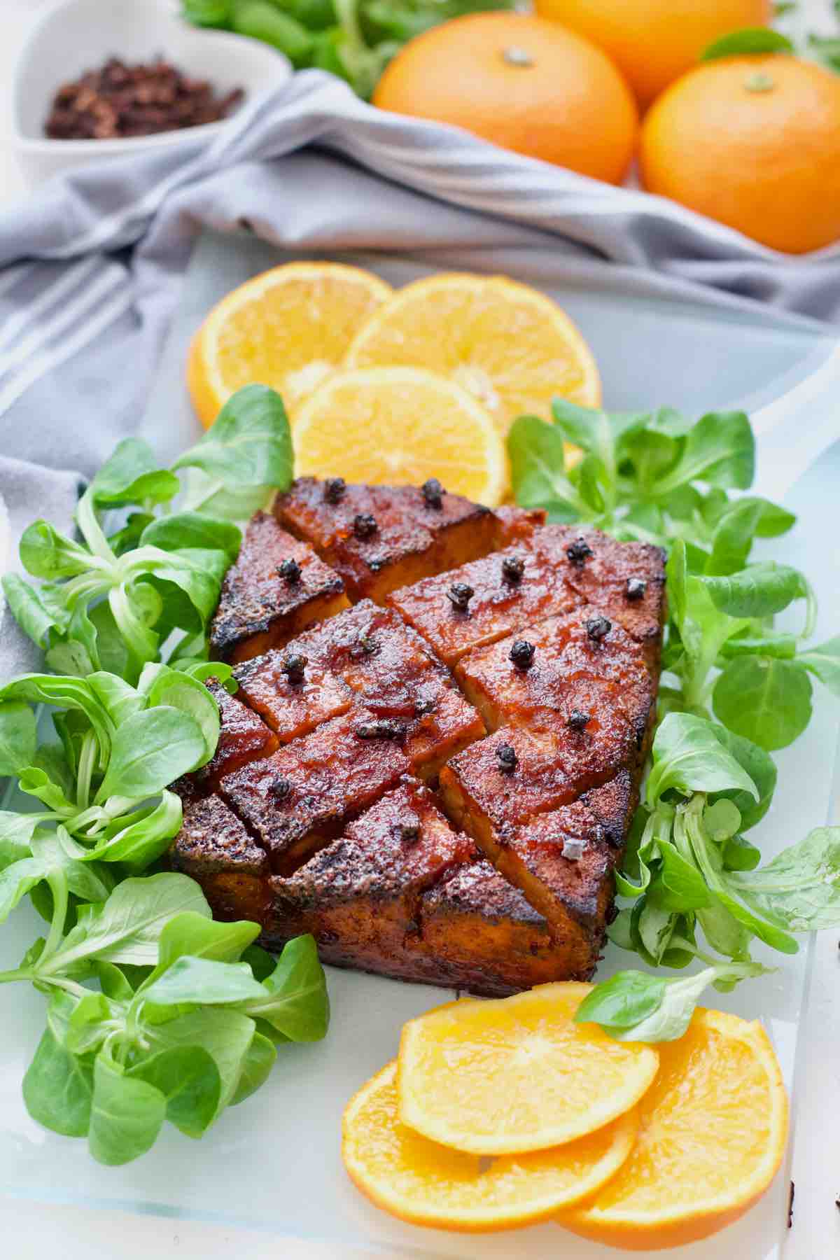 Orange glazed tofu roast on a platter with lamb's lettuce and orange slices.