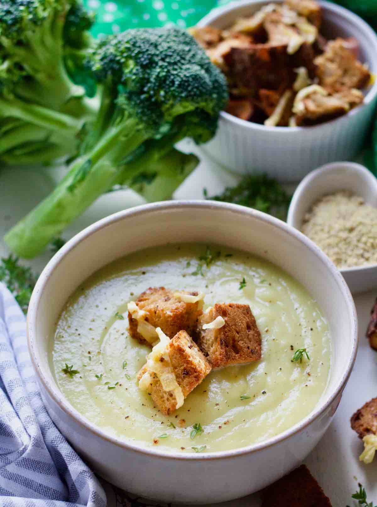 Bowl with soup at the front, broccoli and toppings behind.