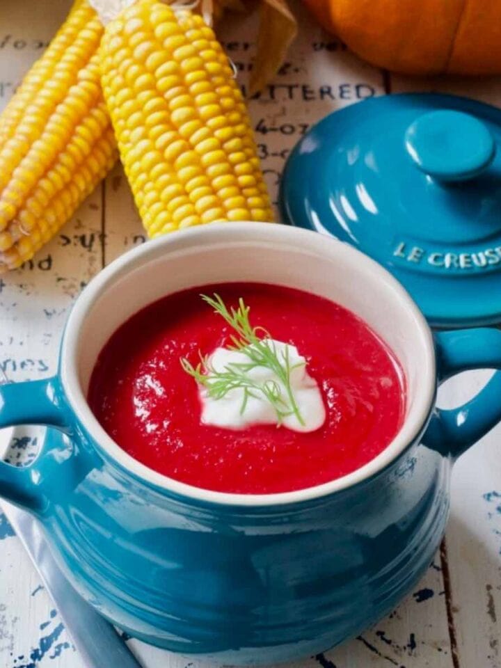 Beetroot soup in a bowl with decorative corn ears behind it.