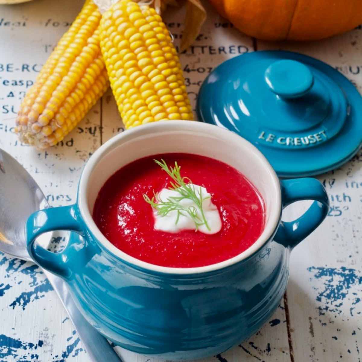 Beetroot soup in a bowl with decorative corn ears behind it.