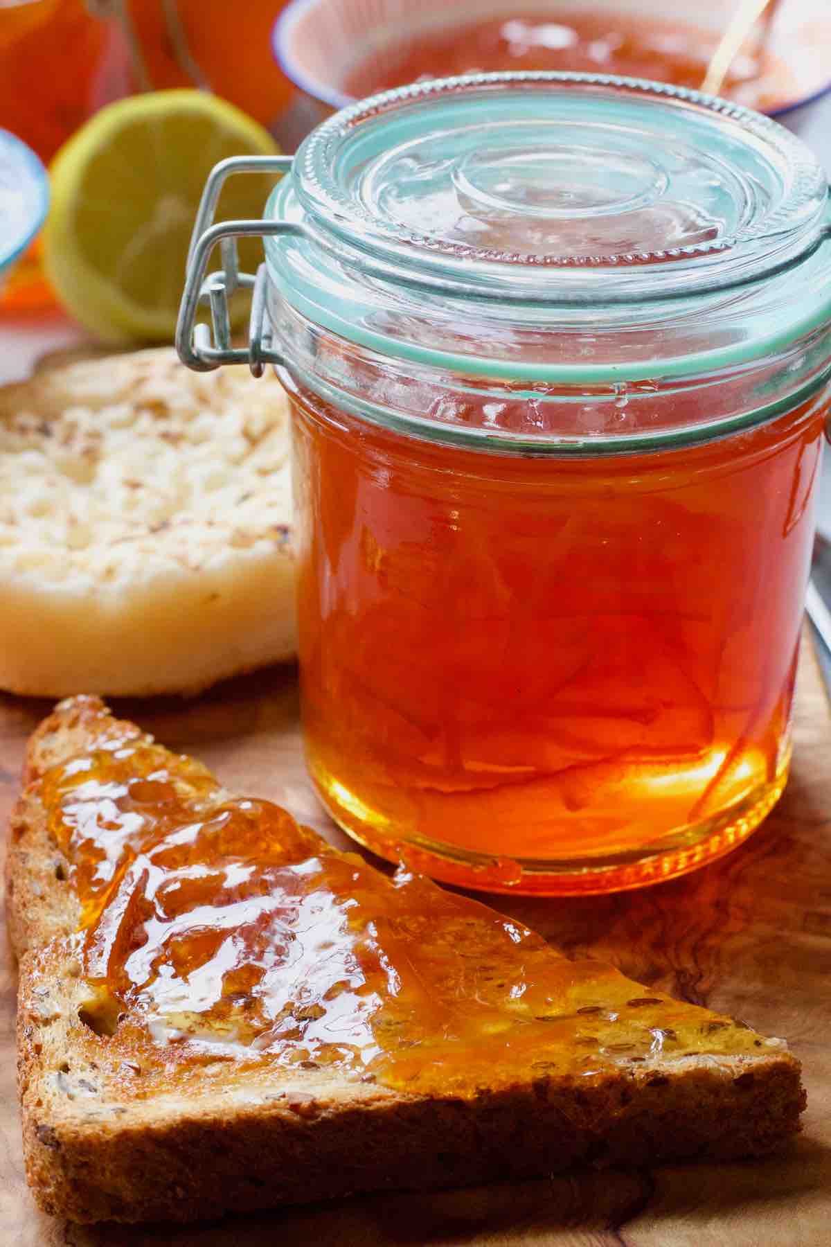 Jar of orange marmalade with piece of toast next to it.