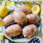 Close up of glazed jagodzianki on a plate with blueberries around.