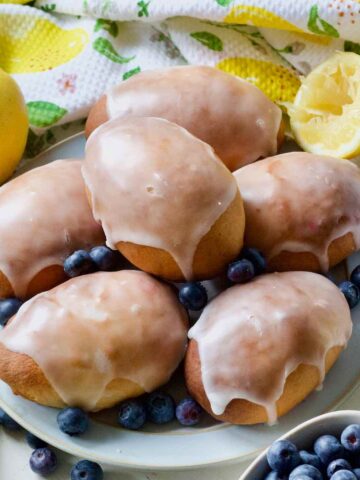 Close up of glazed jagodzianki on a plate with blueberries around.