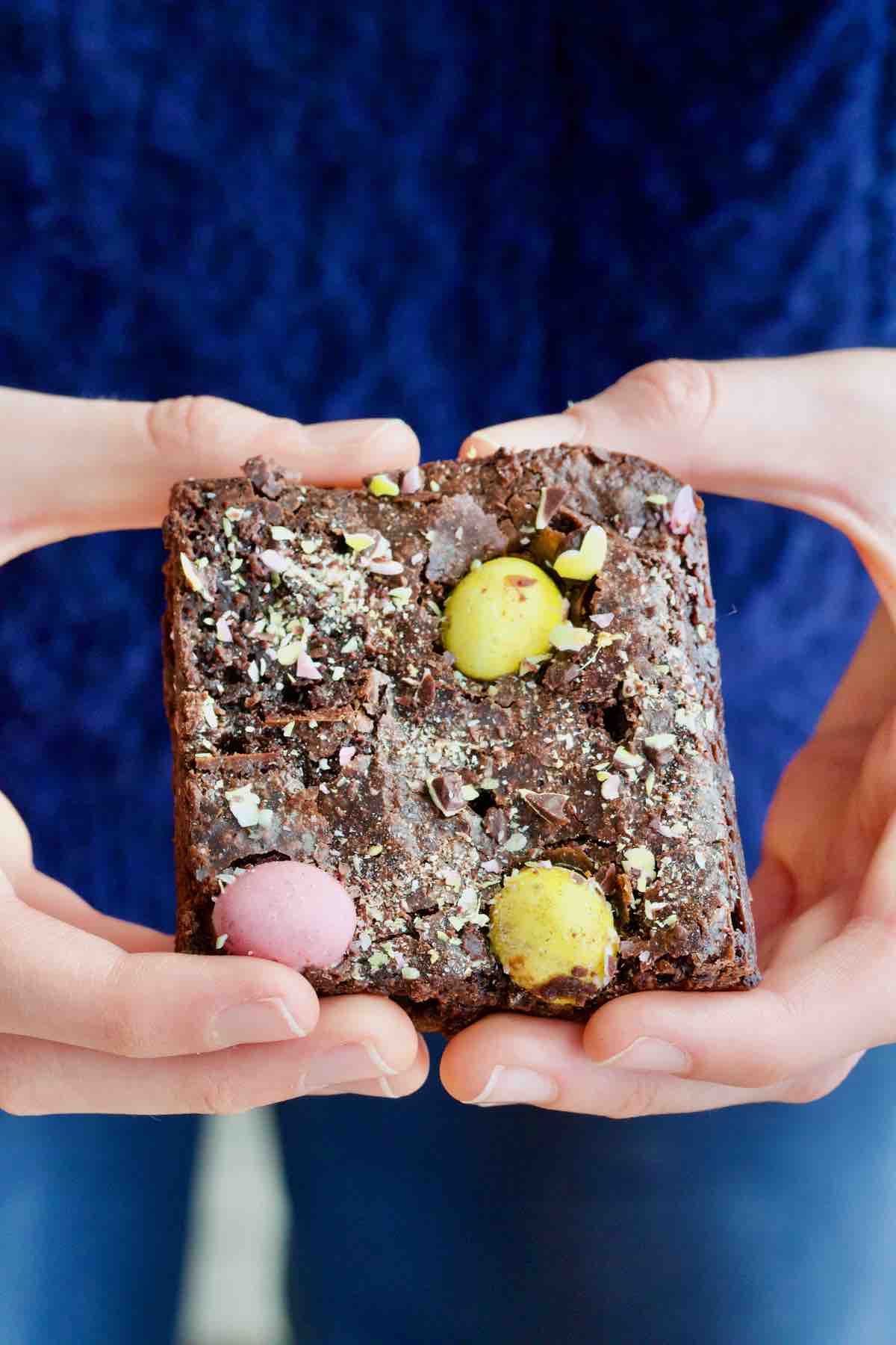 Hands holding one mini egg brownie square.
