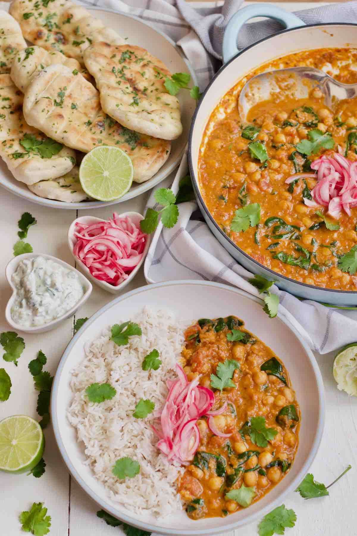 Chickpea and spinach curry spread with naan breads & bowl with curry and rice.