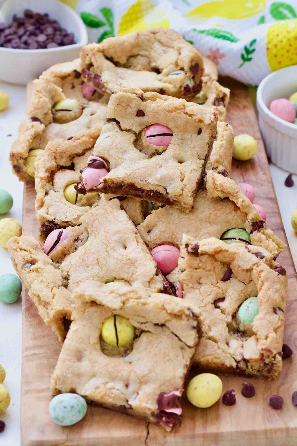 Mini egg cookie bar squares piled up on a board.