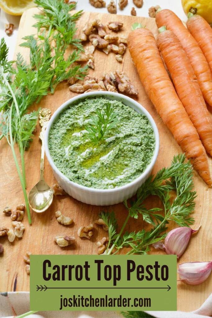 Carrot greens pesto in a bowl surrounded by raw ingredients used to make it.