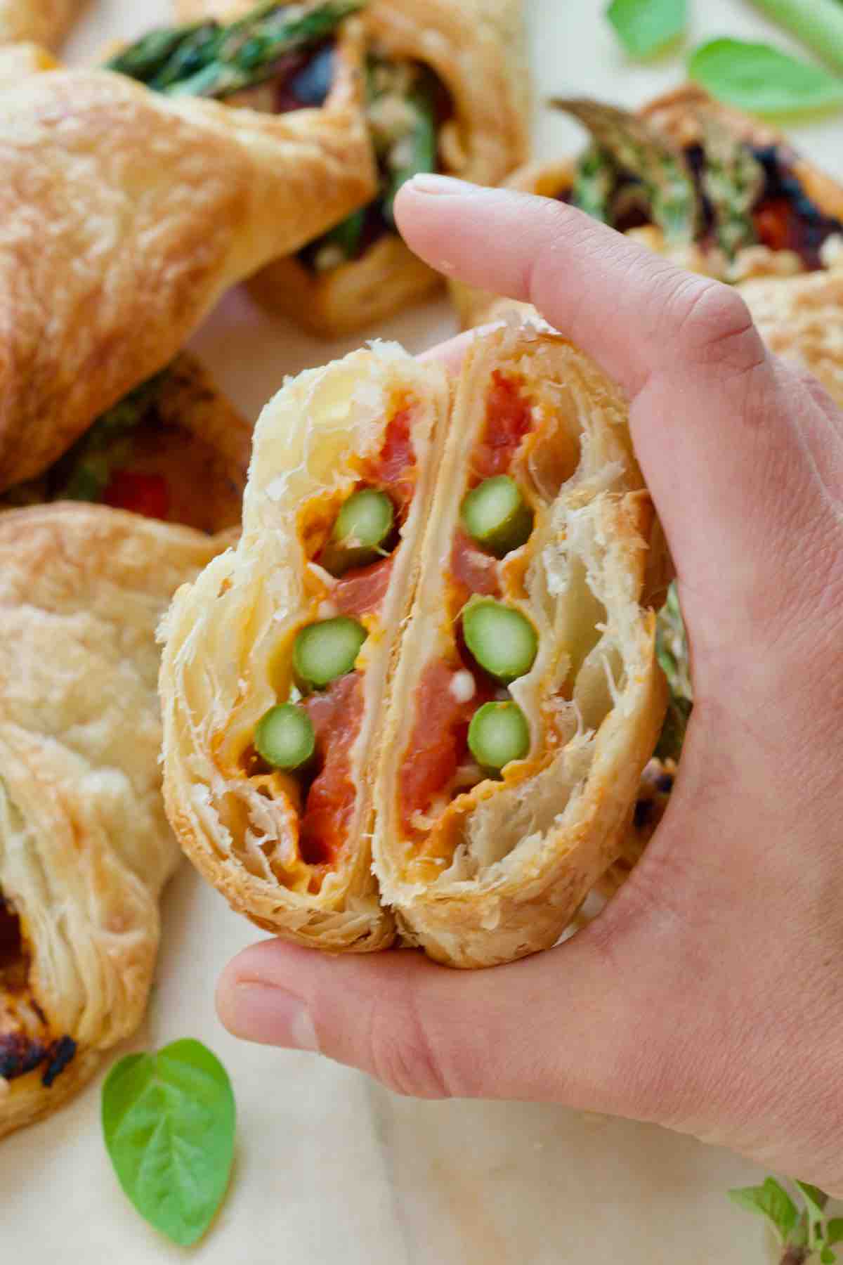 Hand holding asparagus puff pastry bundle cut in half.