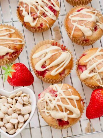 Vegan strawberry muffins on a rack, bowl with white chocolate chips and 2 fresh strawberries.