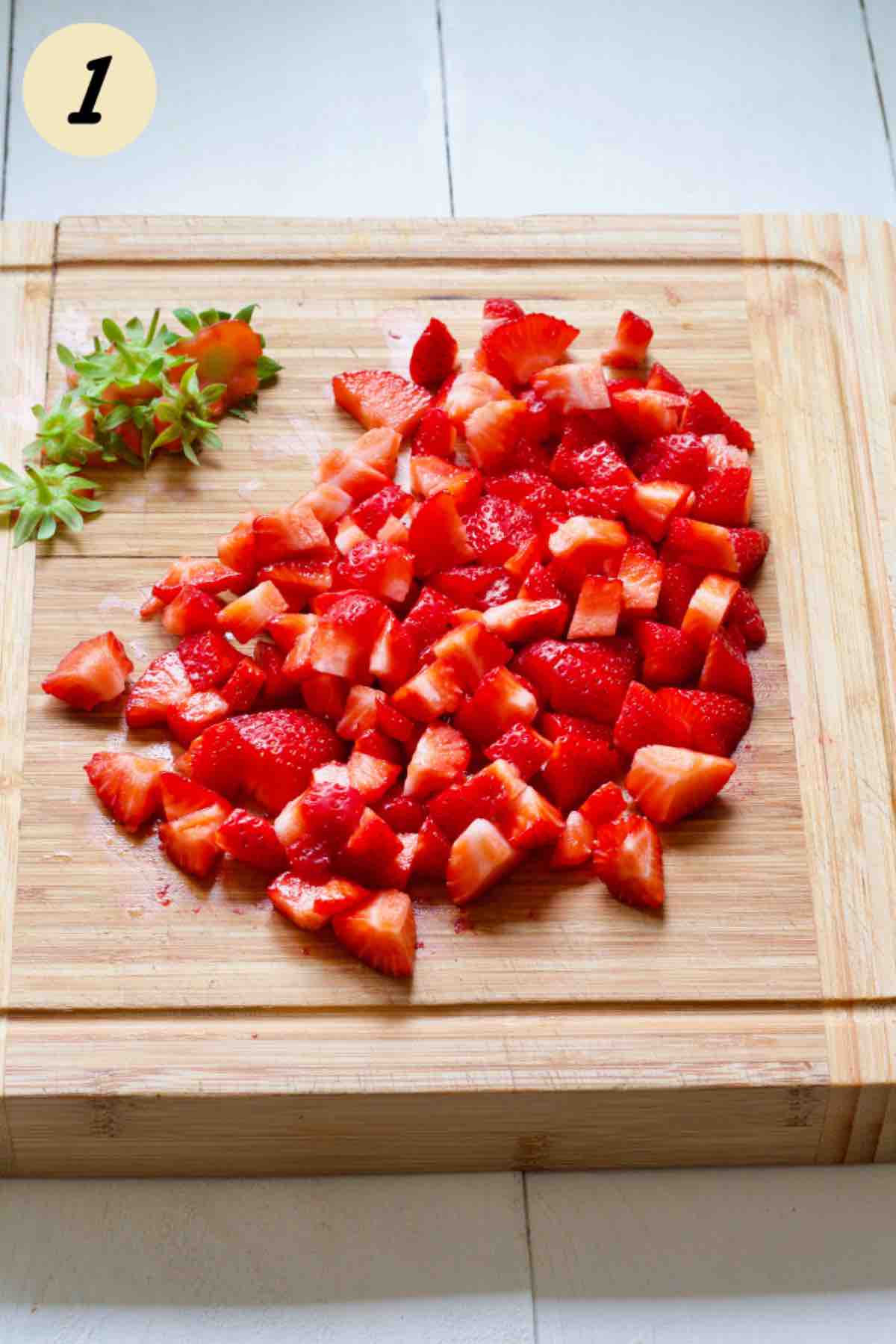 Hulled and chopped strawberries on a wooden board.