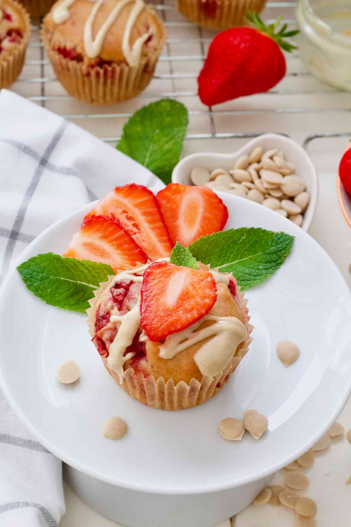 Strawberry muffin on a plate decorated with a slice of strawberry and mint leaves.