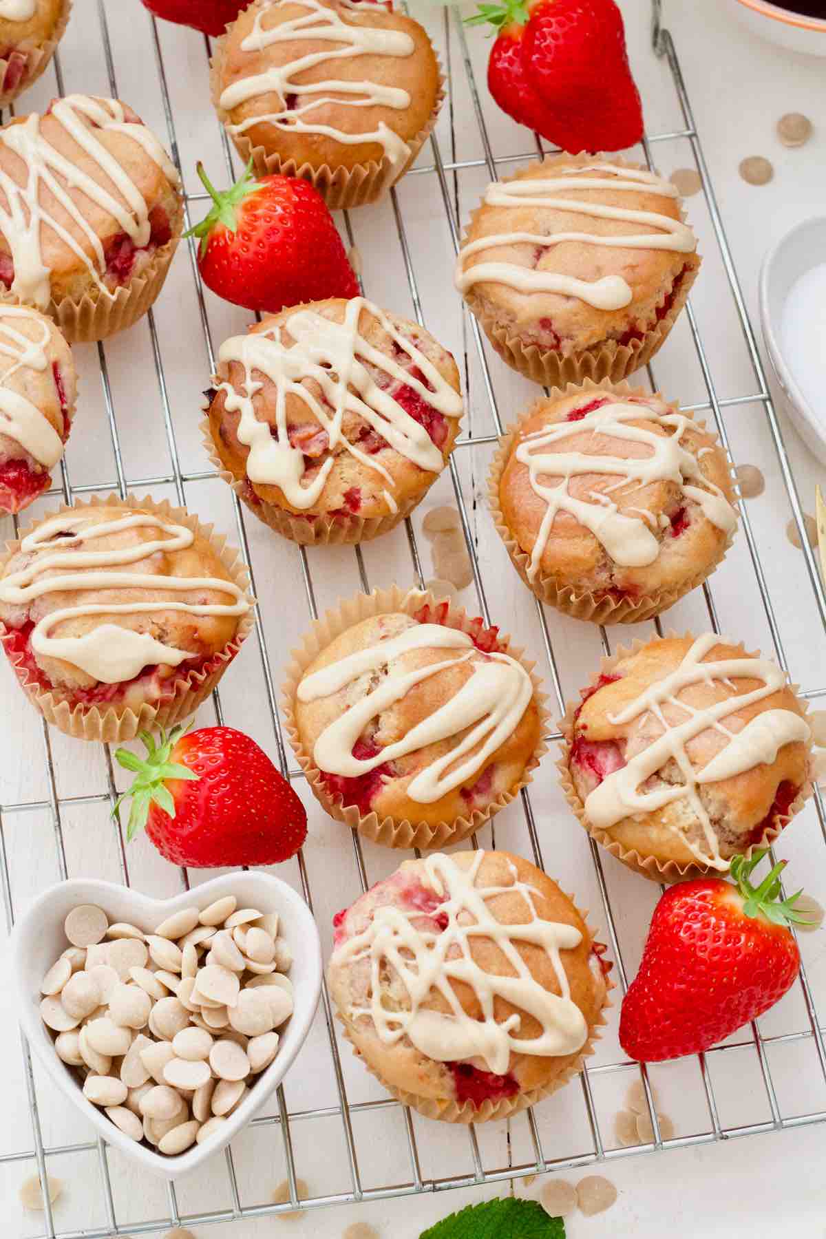 Vegan strawberry muffins with white chocolate drizzle on a cooling rack.