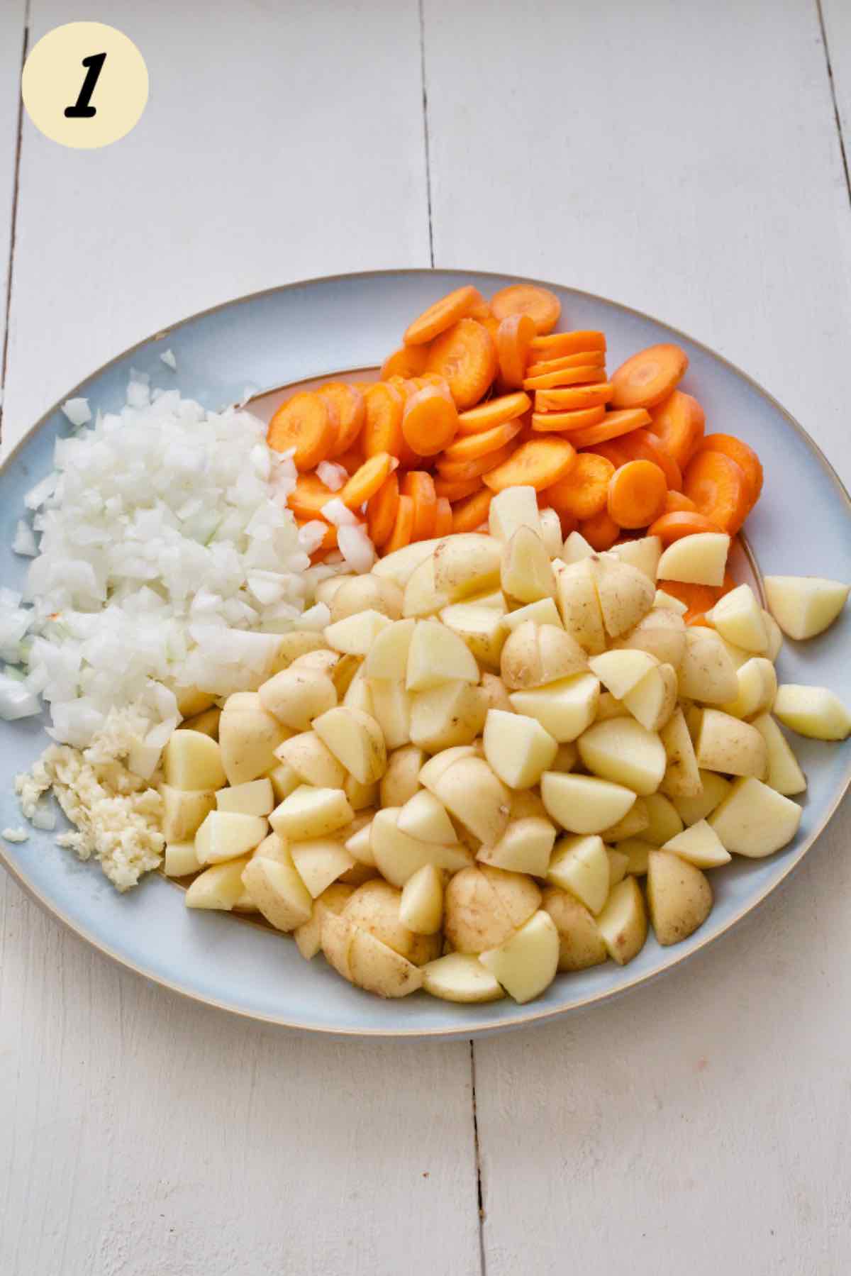 Prepared carrots, potatoes, onion and garlic on a plate.