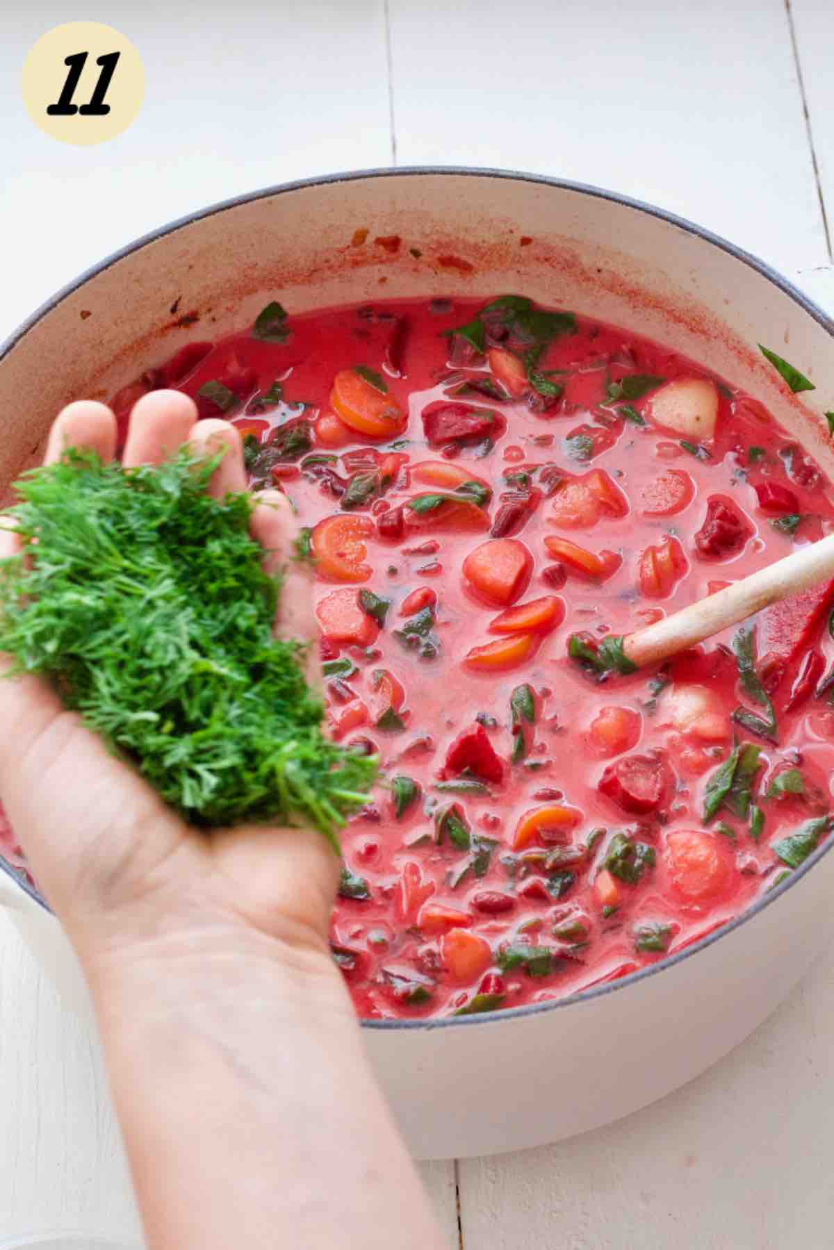 Hand holding chopped dill over the pot of soup.