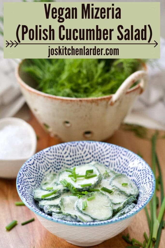 Mizeria in a bowl with green onions, dill and cucumber in a colander behind.