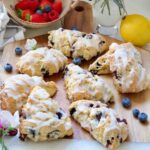 Vegan blueberry scones on a board with blueberries scattered around.