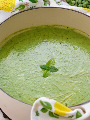 Close up of pot with courgette soup with peas and mint.