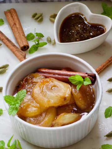 Stewed plums in a bowl and small bowl with sticky syrup behind.