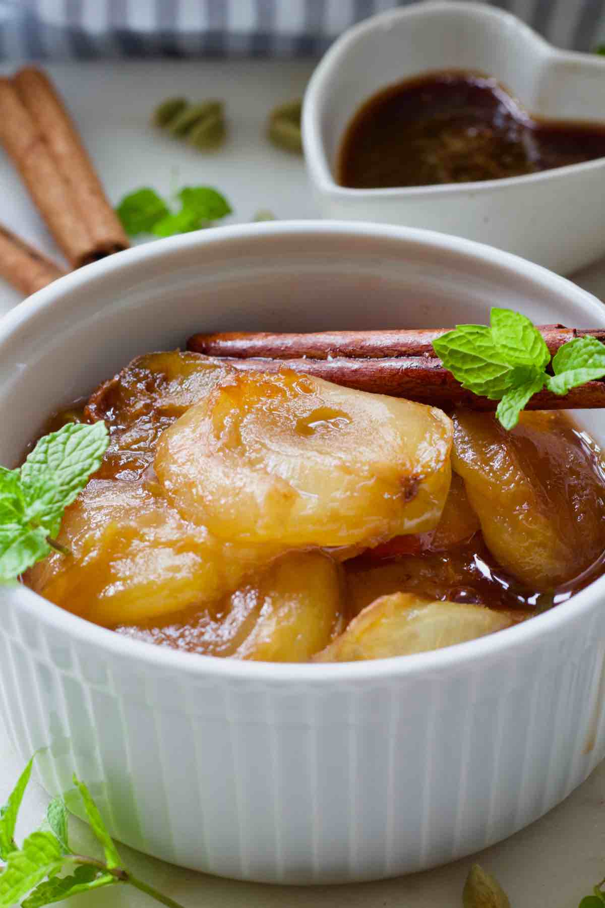 Close up of stewed plums in a bowl with cinnamon stick and mint.