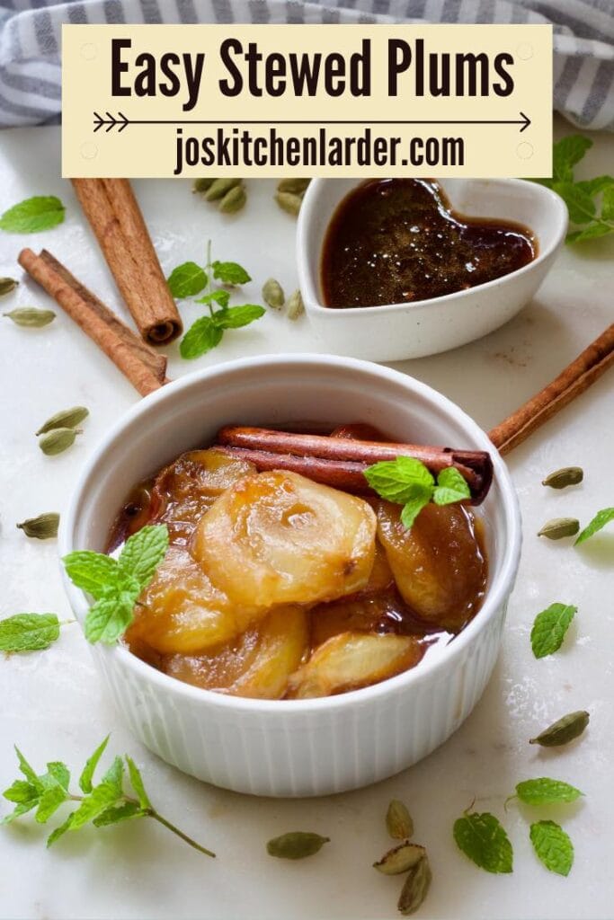 Stewed plums in a bowl, scattered cinnamon sticks, cardamom pods and more mint.