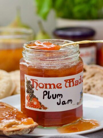 Open plum jam jar with spoon with jam resting over the top of it.