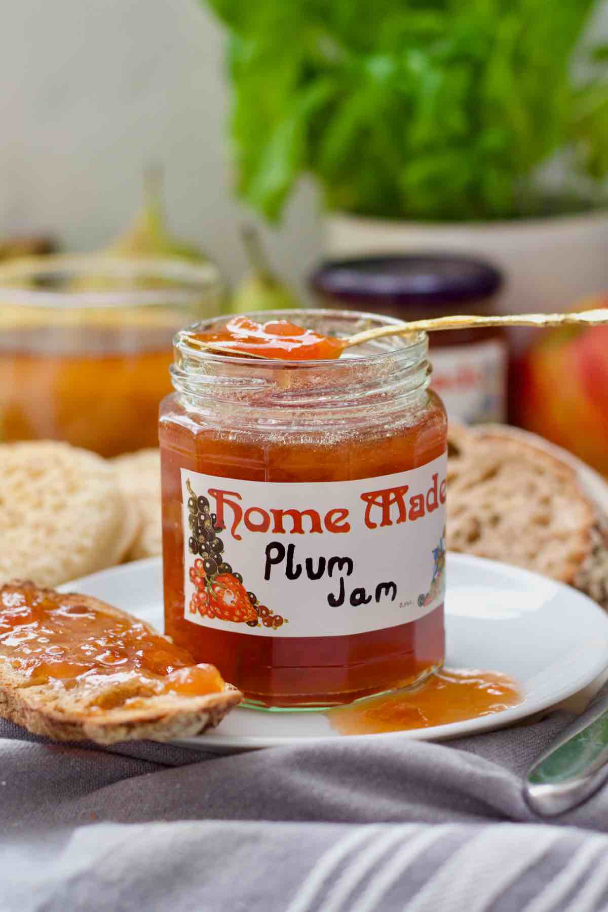 Spoon resting over open jam jar, piece of jam toast and some jam on a plate.