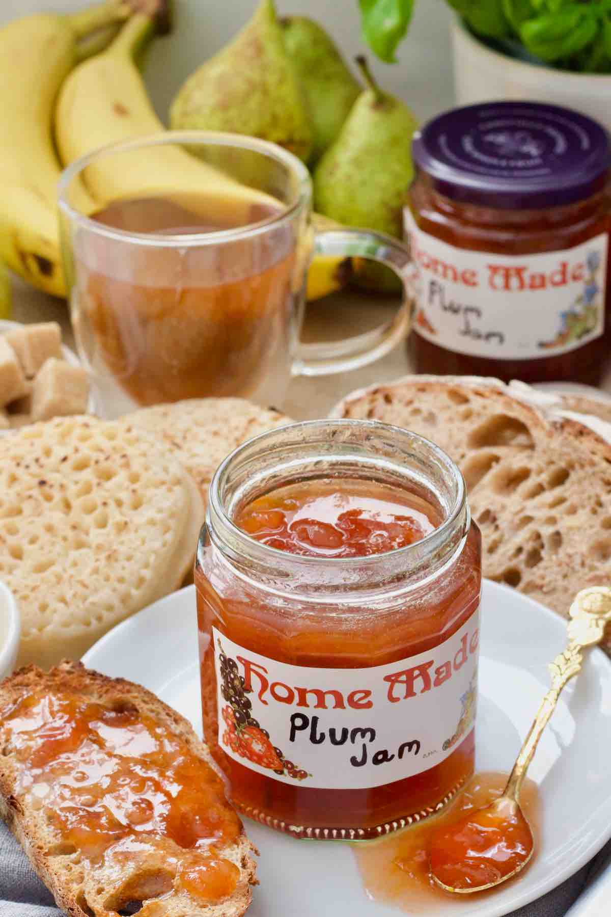 Open plum jam jar on the plate with breakfast spread around.