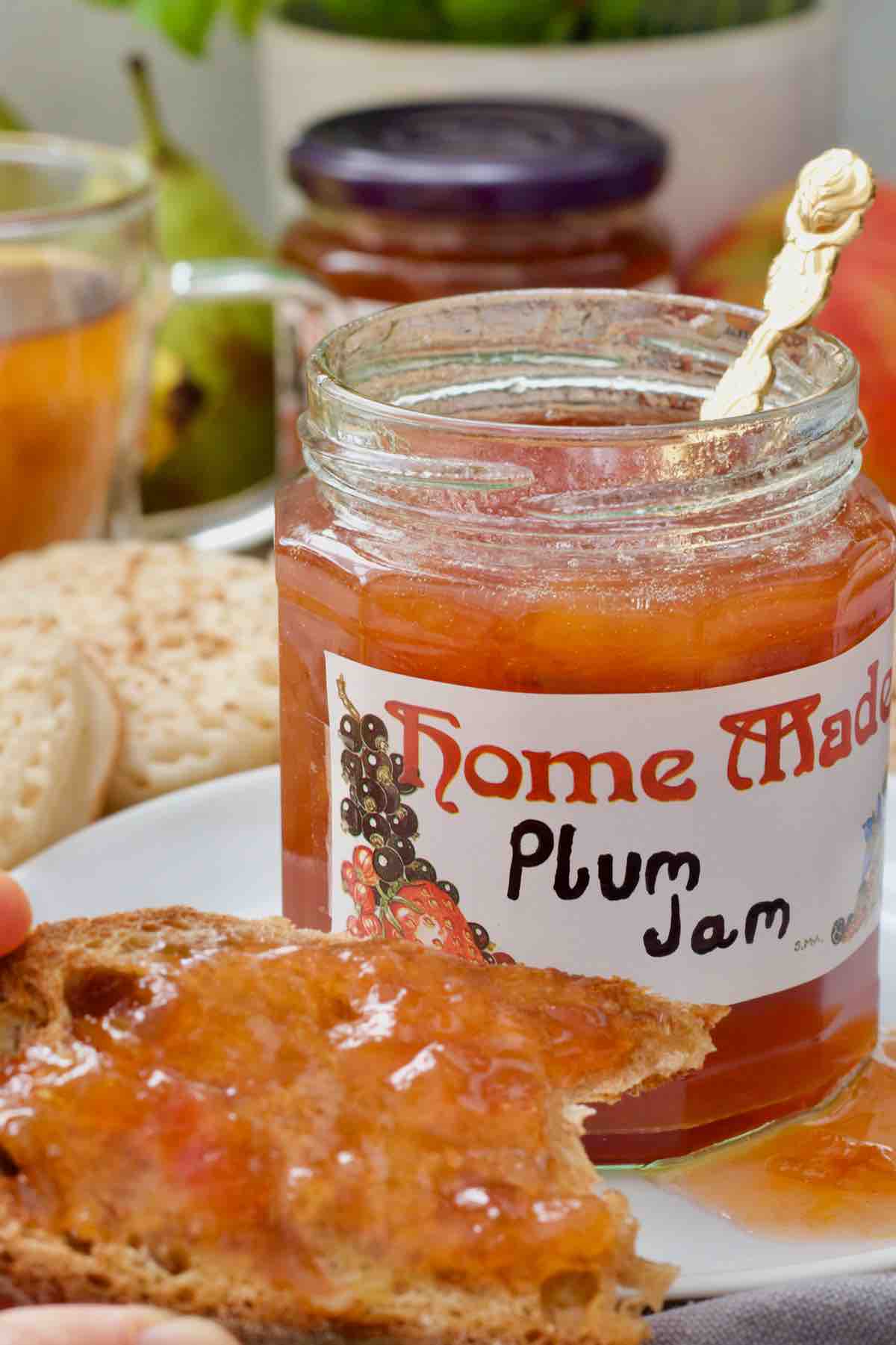 Open plum jam jar with piece of jam toast in front of it.