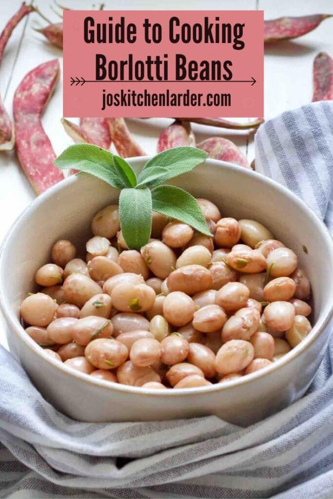 Borlotti beans in a bowl decorated with fresh sage, pods at the back.