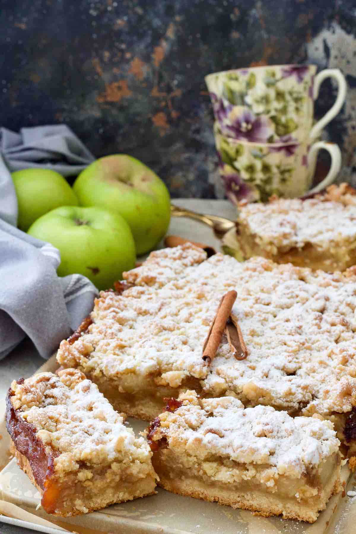 Polish apple cake decorated with cinnamon sticks and with couple of slices cut.