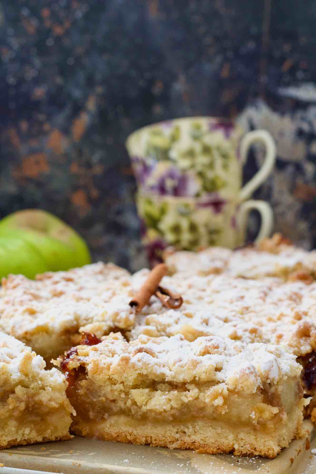 Close up of cut polish apple cake with two tea cups in the background.