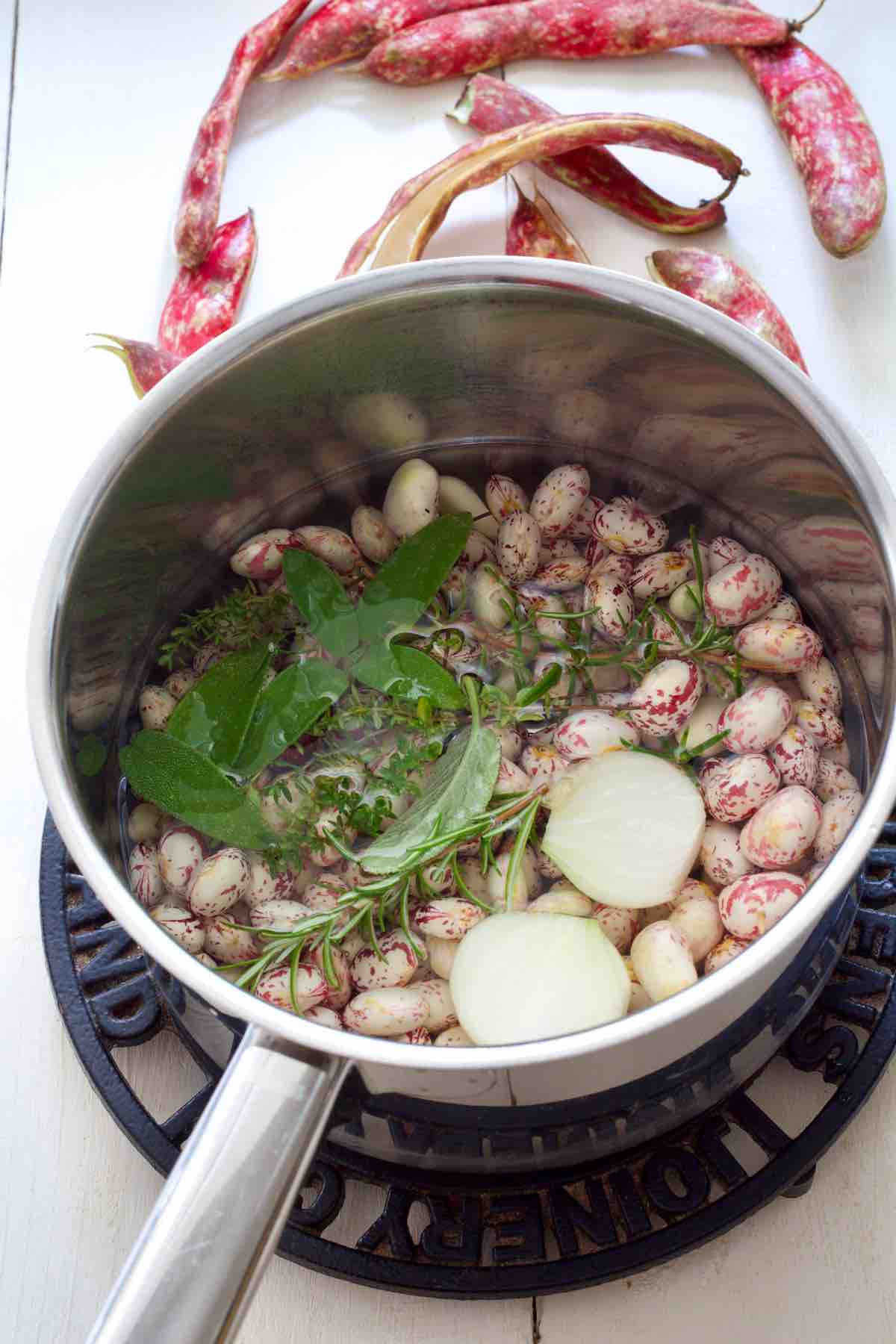Borlotti beans in a pan with water and aromatics before cooking.
