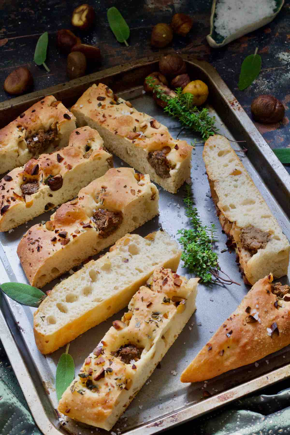 Baking tray full of focaccia slices, herbs and chestnuts.
