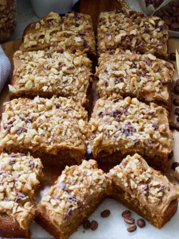 Slices of coffee and walnut cake arranged on a board, coffee beans, sugar cubes and forks.