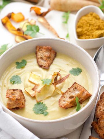 Close up of curried parsnip soup in a bowl with garnishes.