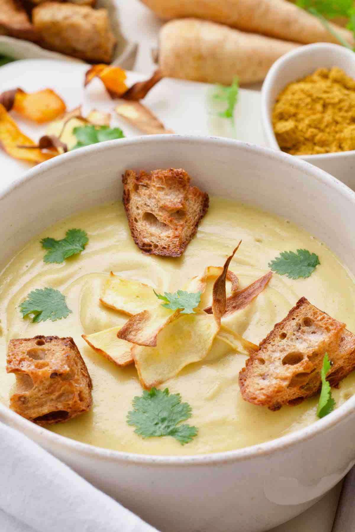 Bowl of curried parsnip soup with croutons, parsnip crisps and coriander.