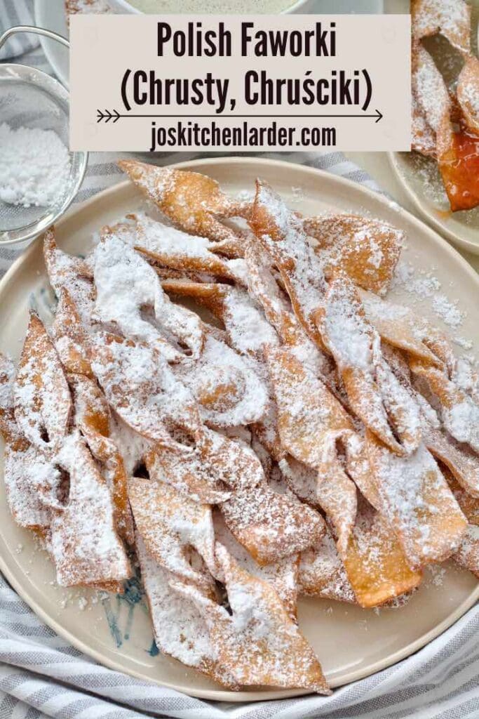 Faworki dusted with icing sugar piled up on the round plate.