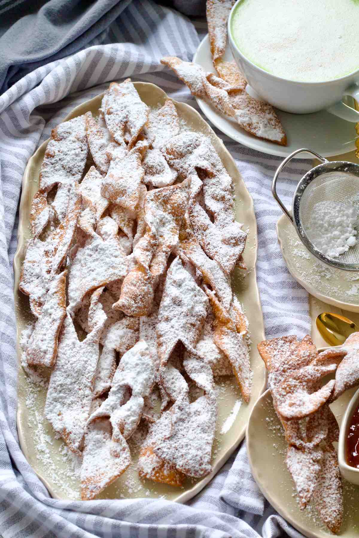 Icing sugar dusted chruściki on an oval shaped platter.