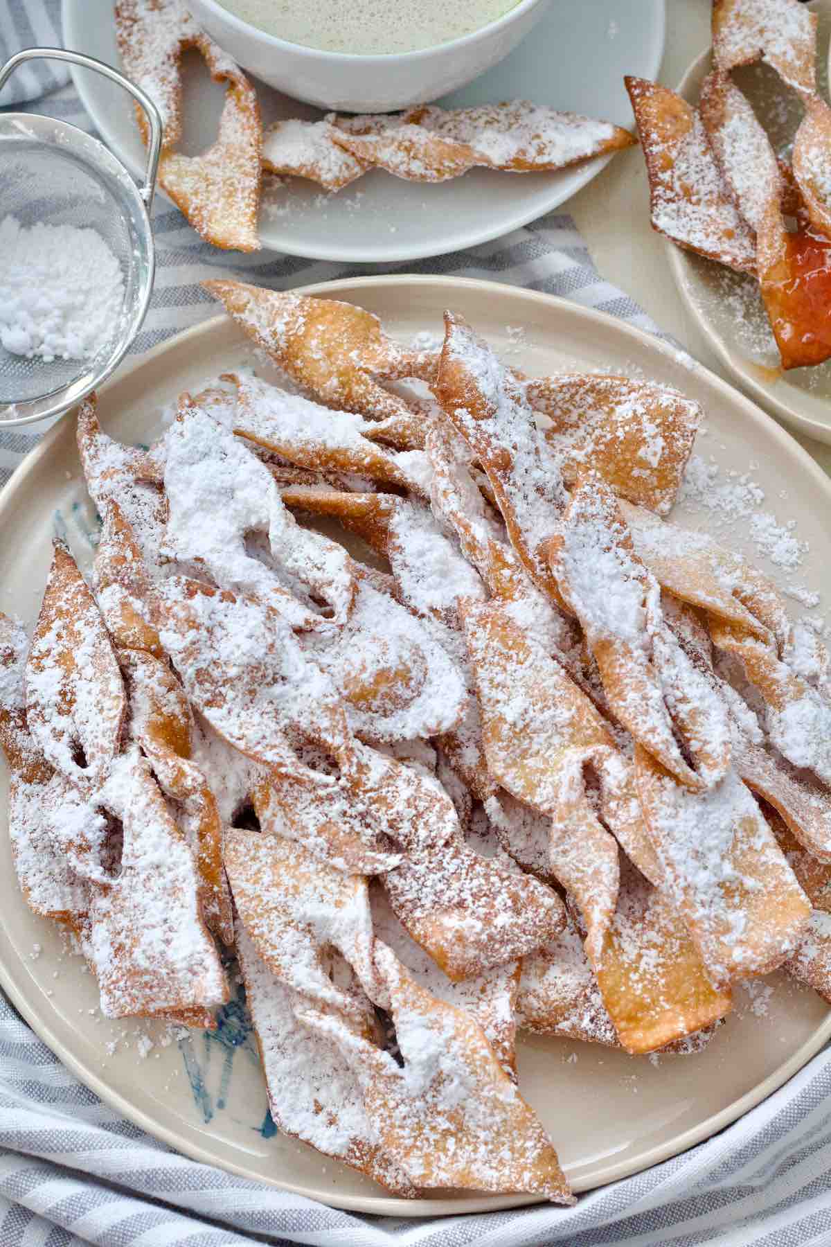 Faworki dusted with icing sugar piled up on the round plate.