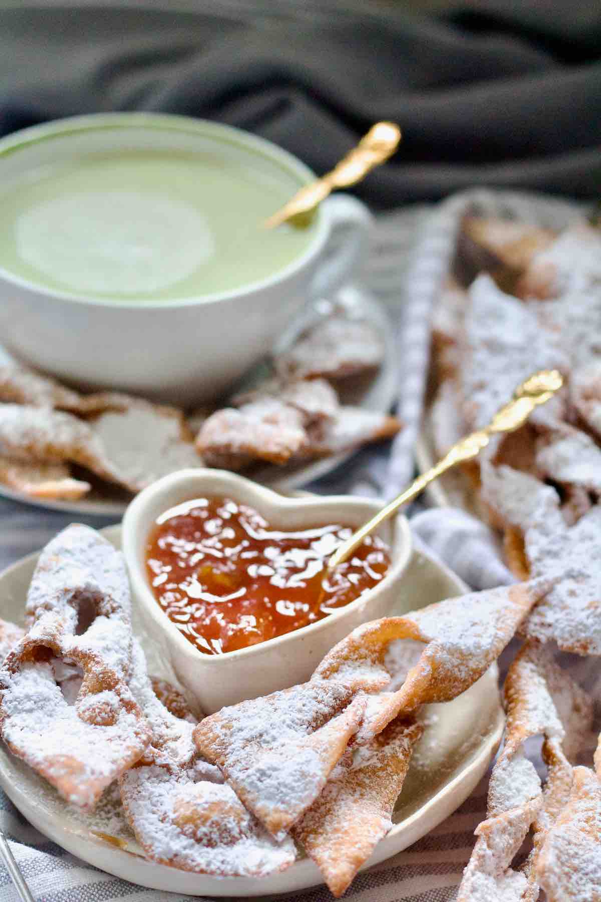 Chrust on a plate with small heart shaped bowl with jam.