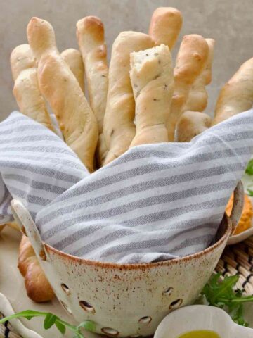 Bunch of breadsticks wrapped in towel in a ceramic colander.