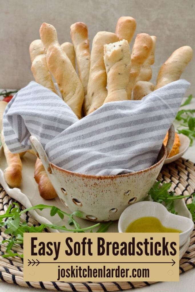 Bunch of breadsticks wrapped in towel in a ceramic colander.