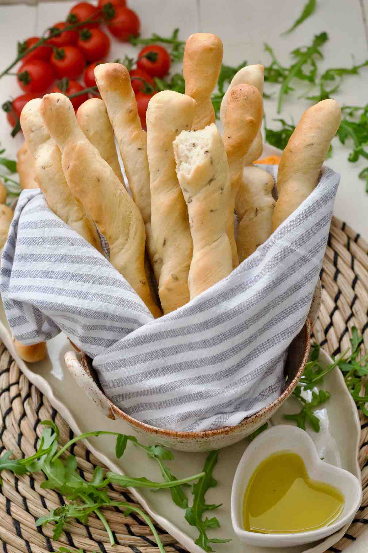 Bunch of breadsticks wrapped in kitchen towel in a serving dish.
