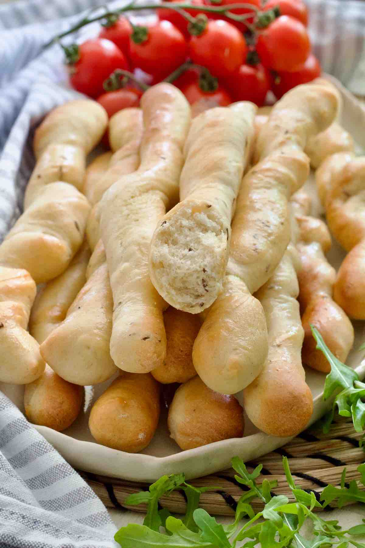 Breadsticks piled up on a platter, cherry tomatoes in the background.
