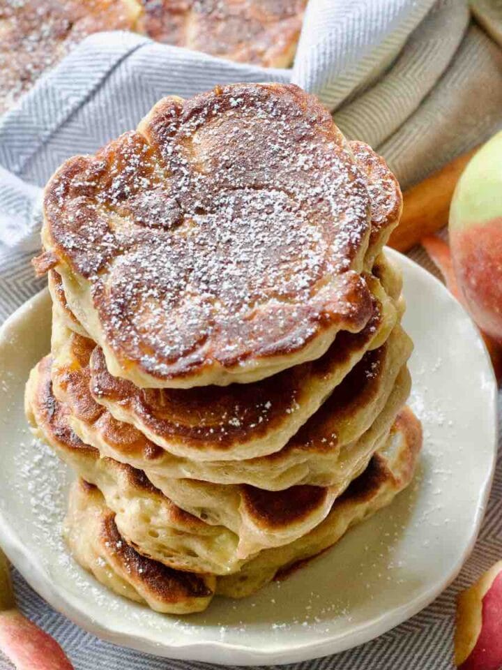 Stack of apple pancakes on a small plate, lightly dusted with icing sugar.