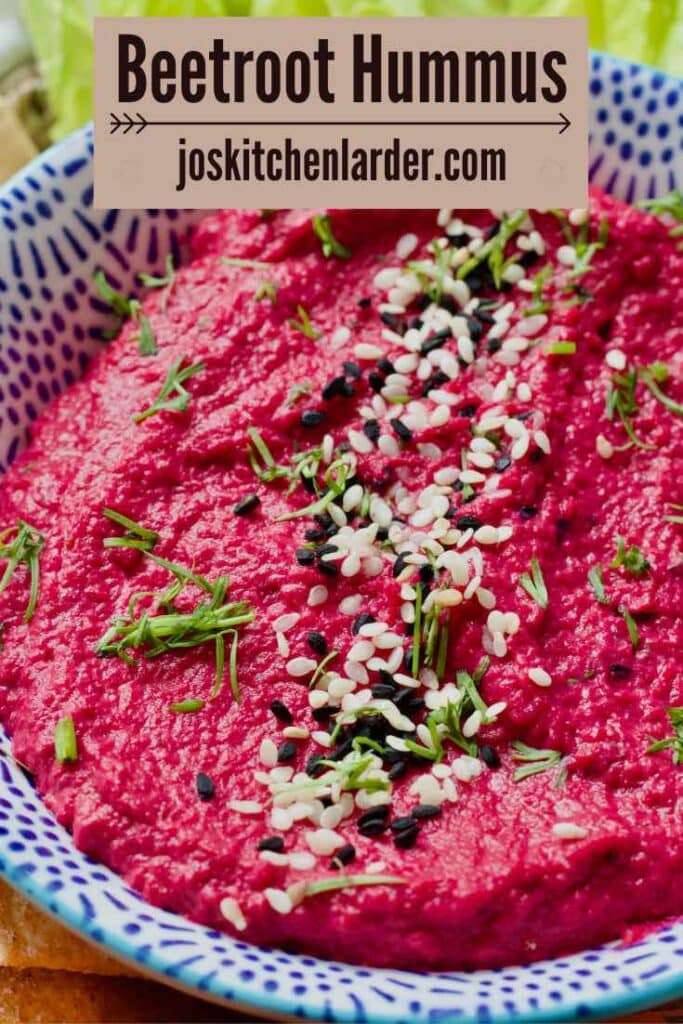 Close up of beetroot hummus in a bowl garnished with sesame seeds and dill.