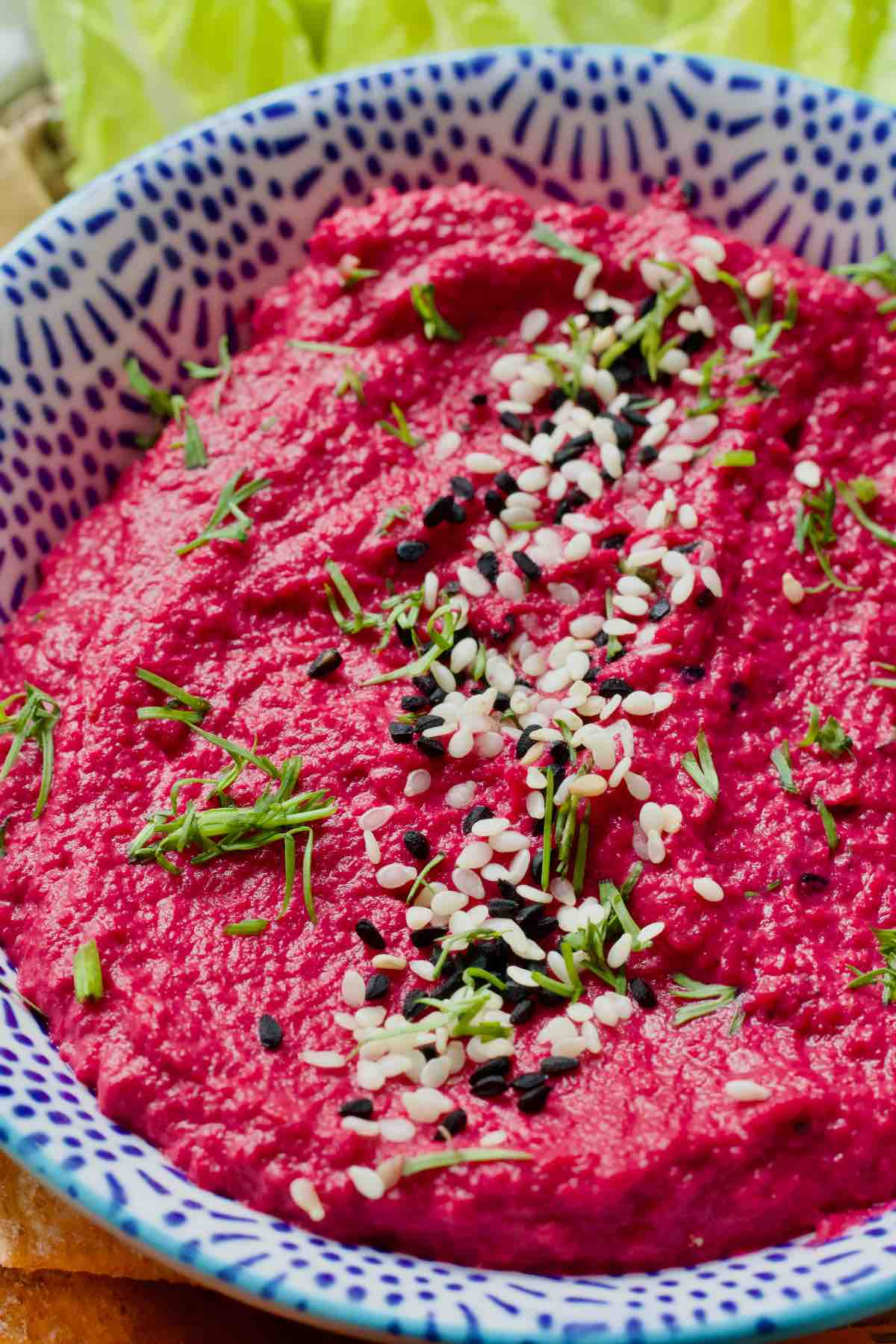 Close up of beetroot hummus in a bowl garnished with sesame seeds and dill.