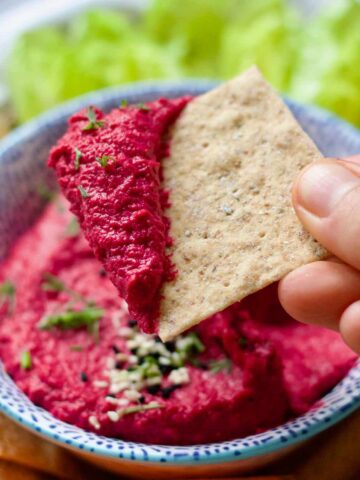 Hand holding a cracker dipped in pink hummus.