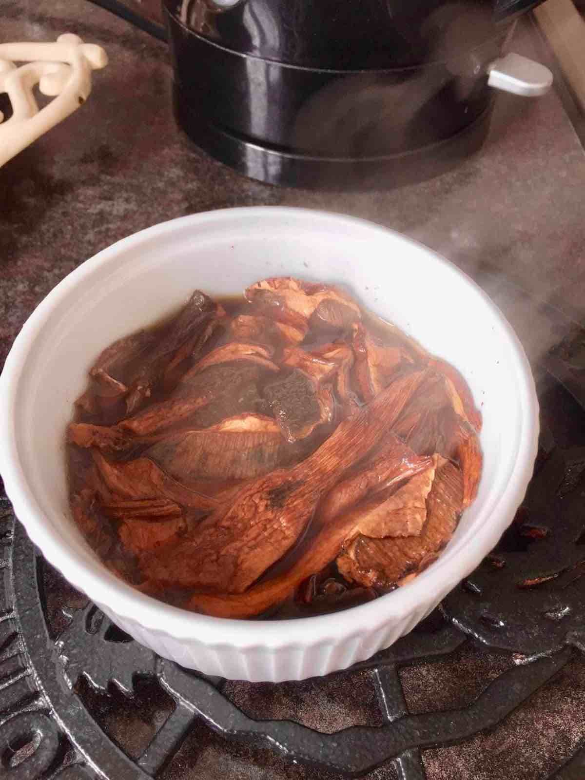 Dried porcini mushrooms in a bowl being rehydrated in hot water.